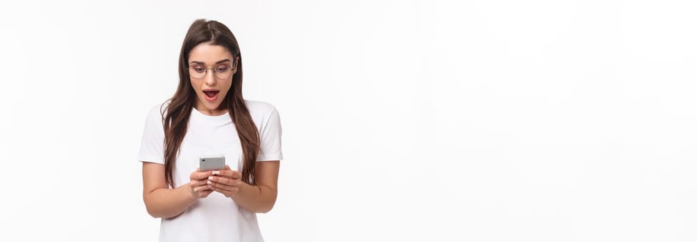 Communication, technology and lifestyle concept. Portrait of surprised and amazed, excited young caucasian woman in glasses, looking at mobile phone, receive awesome new via text message.