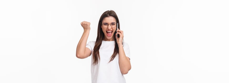Communication, technology and lifestyle concept. Portrait of successful happy and excited woman winning, receive great news on phone, fist pump triumphing and saying yes, hold smartphone near ear.