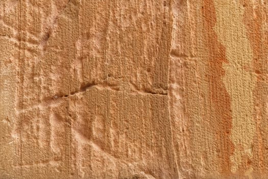 A detailed view of a weathered stone surface showcasing natural textures and vertical striations in shades of orange. The stone has visible grooves and patterns formed over time.