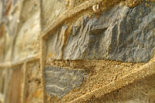 Detailed close-up view of a stone wall with sand grains layered on its surface, highlighting the texture and abstraction of the elements.