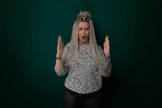 A woman with dreadlocks is standing confidently in front of a vibrant green wall. She is looking directly at the camera, showcasing her unique hairstyle and individuality.