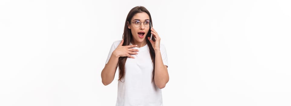 Communication, technology and lifestyle concept. Portrait of excited and surprised, overwhelmed young cute girl receive incredible news, gasping and touching heart as talking on phone, winning.
