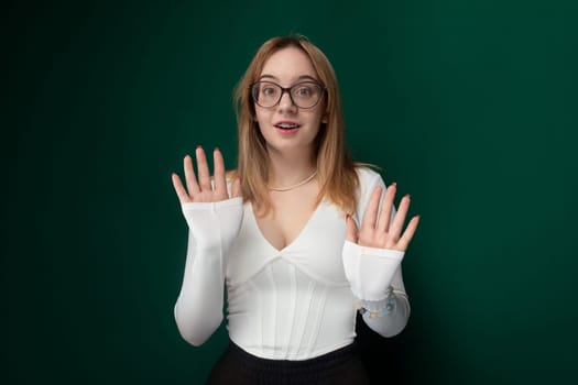 A woman with glasses and a white shirt looking directly at the camera. She has a serious expression on her face, standing in front of a plain background.