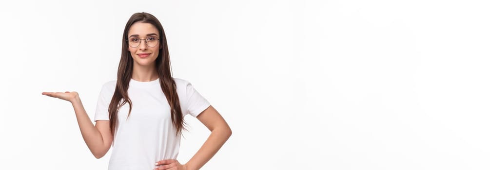 Waist-up portrait of pleasant good-looking caucasian female in glasses, attractive girl holding someone on hand, raising arm as have product on it, smiling camera, advertise, white background.