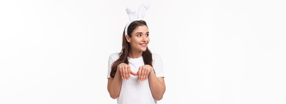 Portrait of funny and cute, playful adult girl in t-shirt and rabbit ears, look away with amused happy face, imitating bunny with paws and silly grin, look away, standing white background.