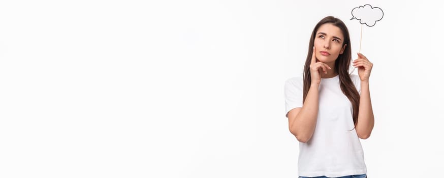 Entertainment, fun and holidays concept. Portrait of thoughtful and creative young woman searching inspiration, holding thinking cloud near head, squinting and look focused up, pondering.