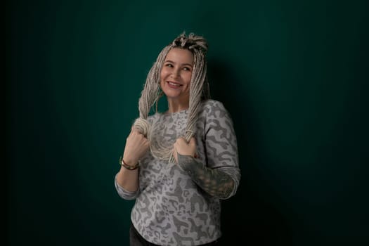 A woman is standing upright in front of a solid green wall, looking directly at the camera. She is dressed in casual attire and appears confident and composed.