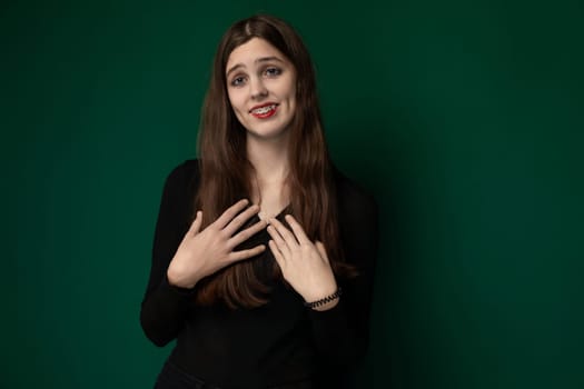 A woman is seen standing directly in front of a solid green painted wall. The woman appears to be looking straight ahead with a neutral expression.