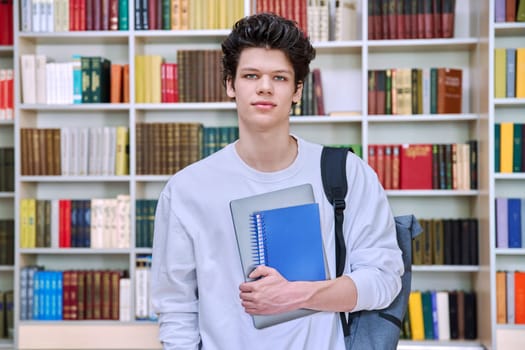 Portrait of confident handsome college student teenage male 19, 20 years old inside library of educational building. Education, youth, lifestyle concept