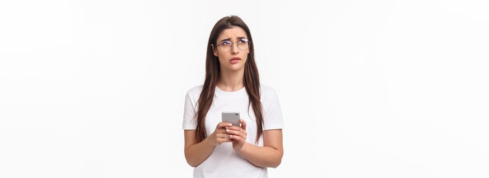 Communication, technology and lifestyle concept. Portrait of troubled and concerned young woman worried for friend, sending text message if shes okay and thinking, look up nervous, hold mobile phone.