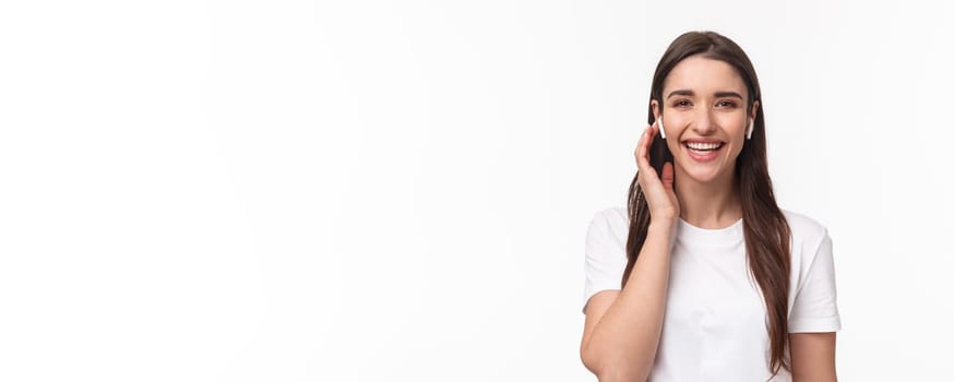 Close-up portrait of attractive smiling happy woman, touching wireless headphone, using earphones to contact friend, having phone conversation with earbuds, laughing carefree.