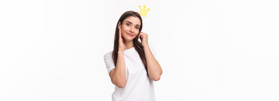 Entertainment, fun and holidays concept. Portrait of beautiful and self-assured charming young smiling woman holding crown on stick near head, feel like princess or queen, white background.