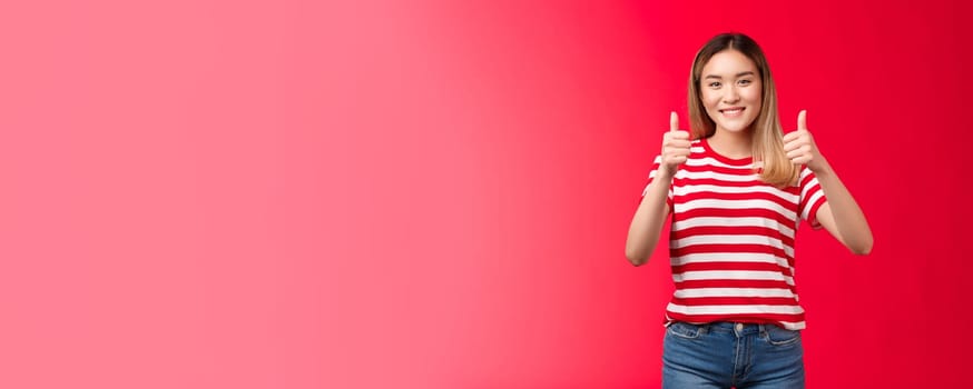 Sounds good have my voice. Cheerful pleasant blond asian girl support friend idea show thumbs-up gesture smiling broadly, female give positive reply, agree approving perfect plan, red background.