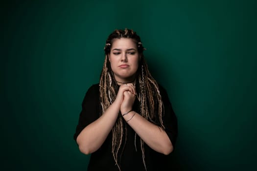 A woman with long dreadlocks stands confidently in front of a vibrant green wall. Her hair is styled in thick, tangle-free dreadlocks, and she appears poised and stylish in her demeanor.