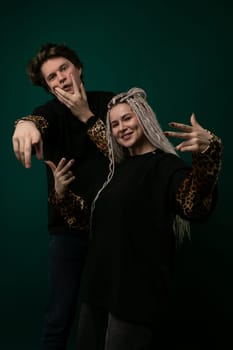 A man and woman are standing together, smiling at the camera as they pose for a photograph. They are in a casual and relaxed pose, with the mans arm around the womans waist. The background is simple, allowing the focus to be on the couple.