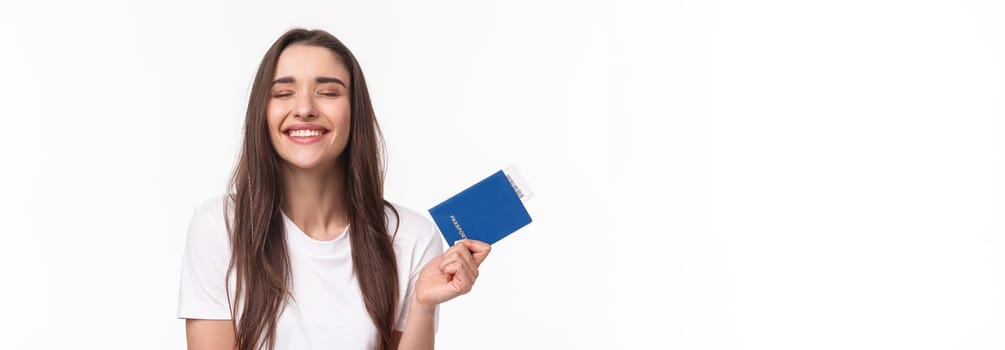 Travelling, holidays, summer concept. Dreamy happy young beautiful girl in white t-shirt, close eyes smiling, daydreaming how she sunbathing near beach on vacation, hold passport with ticket.