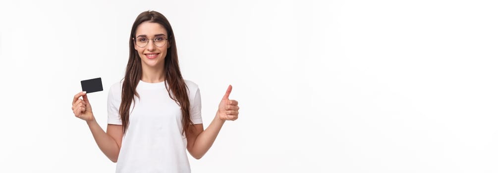 Portrait of confident and happy, smiling young woman in t-shirt, glasses, show thumbs-up and nod in approval, recommend bank, show credit card, buying online with non-cash payment.