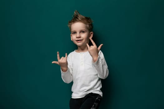 A young male child stands in front of a vibrant green wall, looking directly at the camera with a neutral expression. The boy wears casual clothing and appears to be in an urban environment.