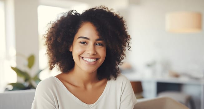 Portrait of beautiful happy smiling young woman looking at camera in white room at home, toothy smile, curly hair