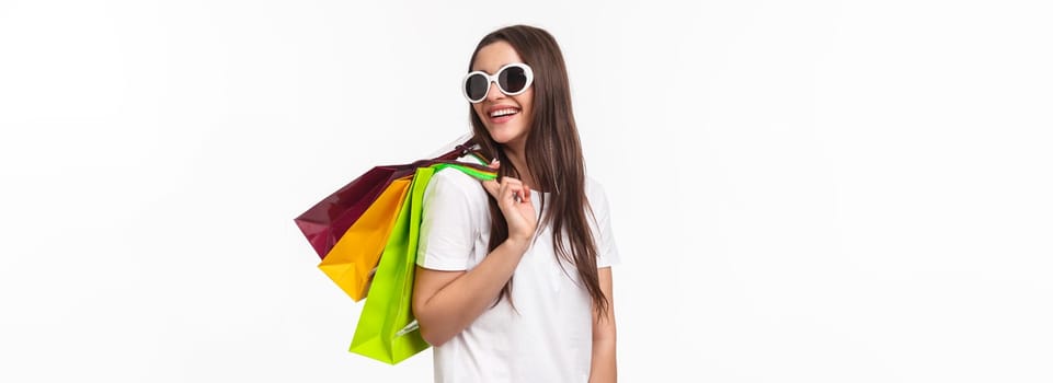 Shopping, leisure and lifestyle concept. Happy, joyful young feminine woman walking in store, buying new clothes and summer bikini, look back with smiling pleased look, hold bags on shoulder.