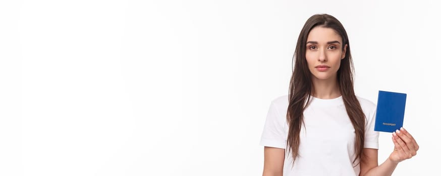 Travelling, holidays, summer concept. Serious-looking young confident girl showing her brand new passport, ready to travel abroad, packing up baggage, standing white background.