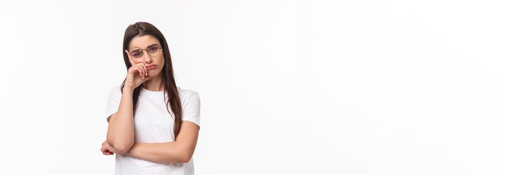 Waist-up portrait of bored, uninterested young brunette female in glasses, feel tired or sleepy, listening to boring conversation, lean on hand look reluctant with lack of interest, white background.