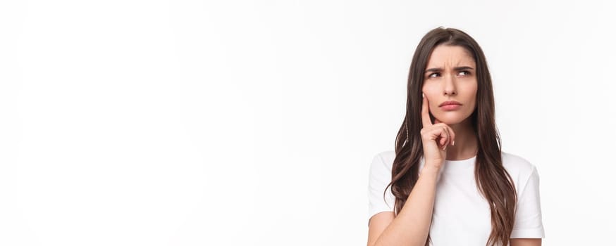 Close-up portrait of serious-looking woman processing situation in mind, looking up frowning doubtful, having hesitating feeling, thinking touching face, standing white background pondering.