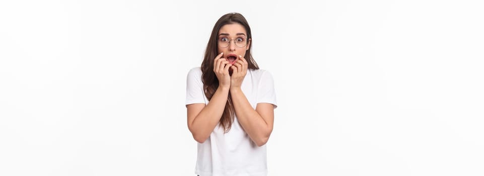 Waist-up portrait of shocked, overwhelmed and panicking young woman worried about breaking news about virus situation, hold hands near mouth frightened, express fear, look startled.