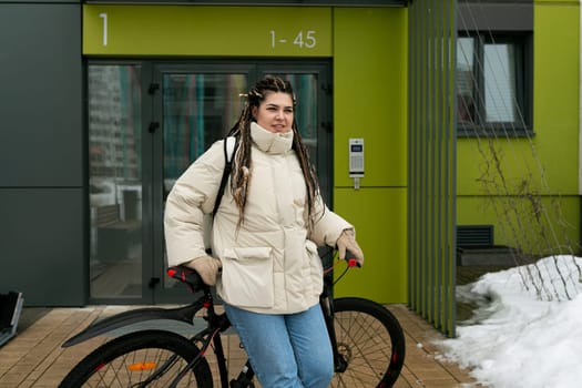 A woman with dreadlocks is standing next to a bike. She appears to be examining the bike, possibly before going for a ride. The woman is dressed casually, and the setting seems to be outdoors.