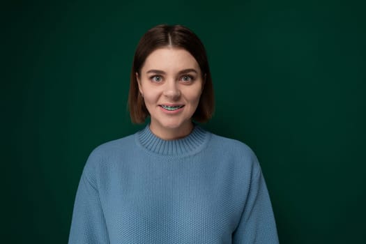 A woman wearing a blue sweater is striking a pose for a photograph. She is standing confidently with a slight smile on her face, her hands gracefully positioned. The background is simple, allowing the focus to remain on the woman and her outfit.