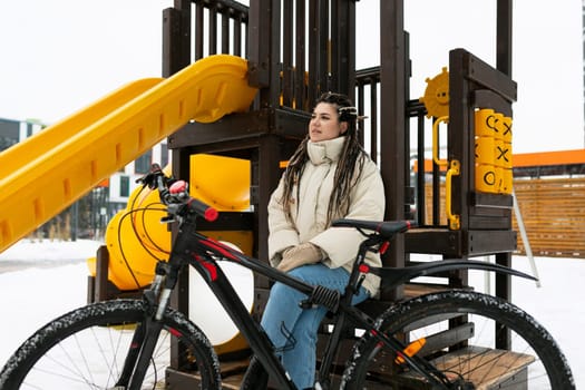 A woman is seated on a bench next to her bike, looking relaxed. The scene captures a simple moment of rest during a bike ride.