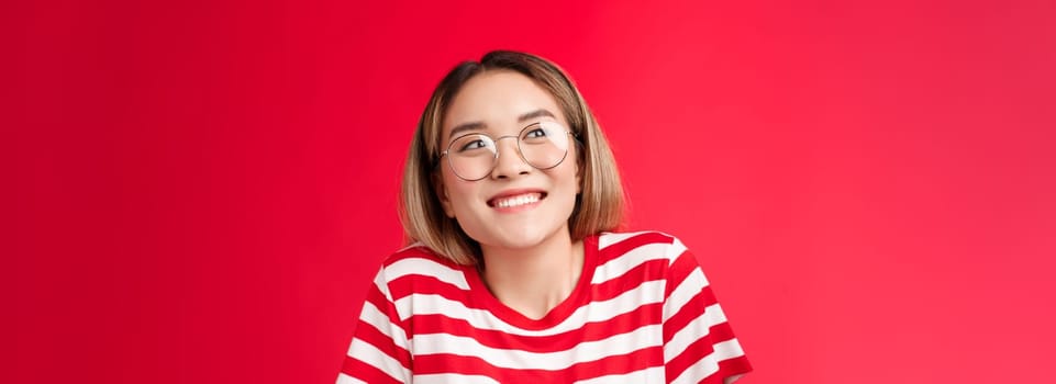 Cheerful silly cute asian girlfriend cannot wait show boyfriend b-day present smiling broadly thrilled look away pondering, thinking about pleasant happy moment, dreaming stand red background.