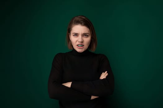 A woman standing with her arms crossed in front of a vibrant green background, showcasing a confident posture. The green backdrop contrasts with the womans stance, creating a visually striking image.