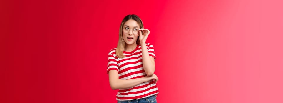 Attractive creative blond asian female journalist got great idea wear glasses check eyewear nose look up intrigued, pondering plan making assumptions, stand red background curious and intrigued.