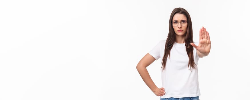 Waist-up portrait of serious-looking displeased confident young woman in glasses, activist or human-rights supporter pull palm forward to stop something bad, frowning disagree, prohibit action.