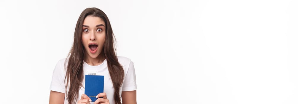 Travelling, holidays, summer concept. Close-up portrait of impressed, shocked young woman holding passport, drop jaw and staring astonished at camera, ready to travel, moving abroad.