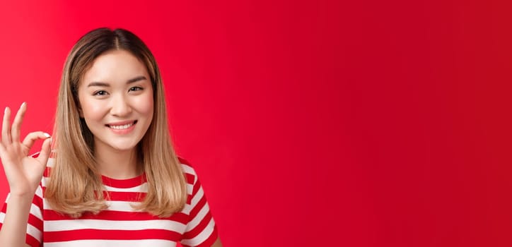 Close-up friendly satisfied carefree young asian blond girl show approval judgement sign okay ok, agree plan good smiling broadly like your idea satisfied great choice, stand red background glad.