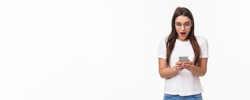 Communication, technology and lifestyle concept. Portrait of surprised and amazed, excited young caucasian woman in glasses, looking at mobile phone, receive awesome new via text message.