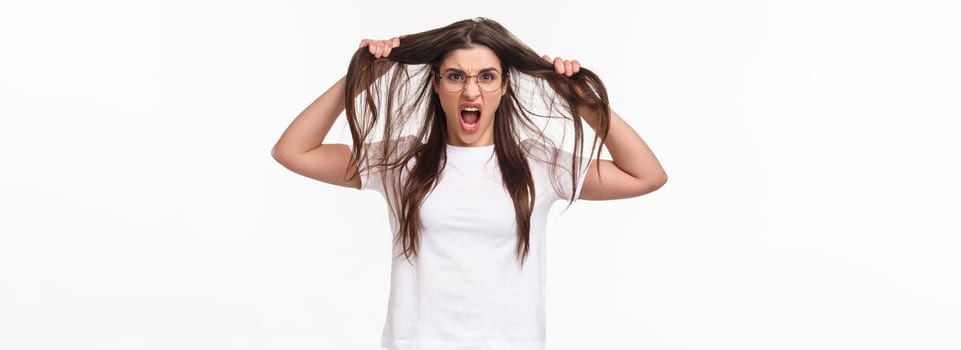 Waist-up portrait of bothered and annoyed, angry pissed-off young girlfriend losing temper, pulling hair from head and screaming being furious and outraged, white background.