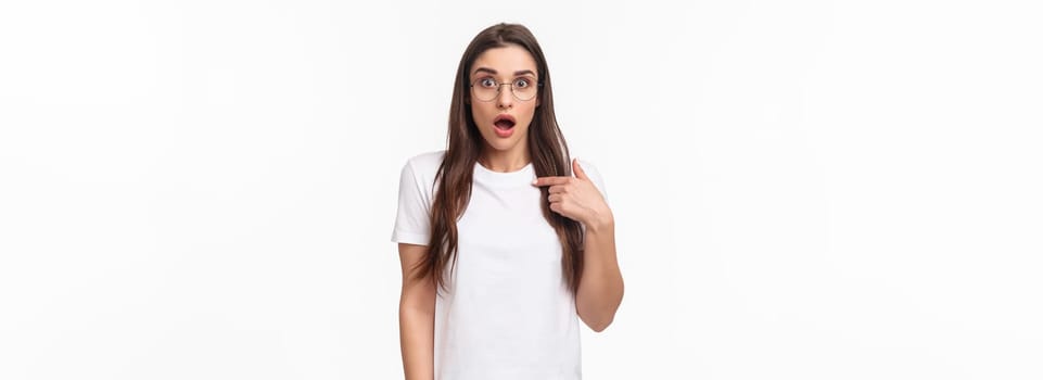 Portrait of surprised, startled young brunette female 20s in glasses, pointing at herself gasping and open mouth, widen eyes staring camera, being mentioned or chosen, picked from crowd.