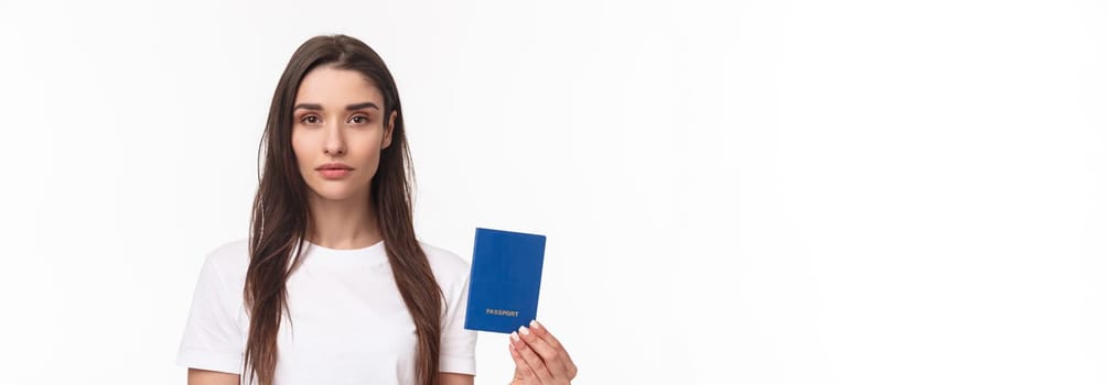 Travelling, holidays, summer concept. Serious-looking young confident girl showing her brand new passport, ready to travel abroad, packing up baggage, standing white background.