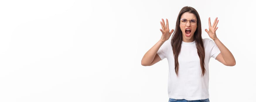 Waist-up portrait of angry, pissed-off brunette pretty girl in glasses, shouting, blaming partner for cheating on her, shaking hands and screaming, having confrontation, frowning aggressive.