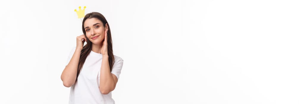 Entertainment, fun and holidays concept. Portrait of beautiful and self-assured charming young smiling woman holding crown on stick near head, feel like princess or queen, white background.