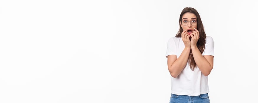 Waist-up portrait of shocked, overwhelmed and panicking young woman worried about breaking news about virus situation, hold hands near mouth frightened, express fear, look startled.