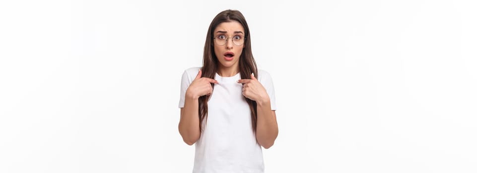 Waist-up portrait of nervous, surprised and silly young 20s woman in glasses, pointing at herself anxiously looking with opene mouth at camera, being worried as picked for mission.