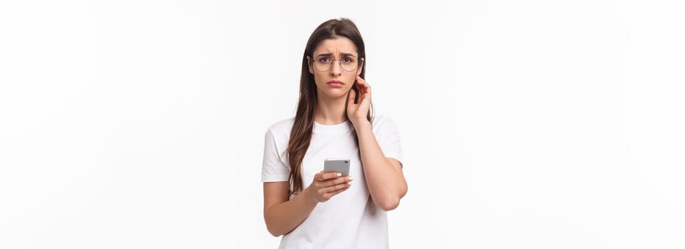 Communication, technology and lifestyle concept. Waist-up portrait of gloomy, sad young brunette in glasses, frowning and sighing upset, holding mobile phone, receive bad awful news, smartphone.