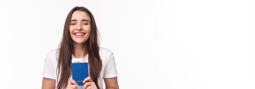 Travelling, holidays, summer concept. Close-up portrait of happy, dreamy girl feeling happy finally travel, holding passport with plane ticket, waiting in airport, standing white background.