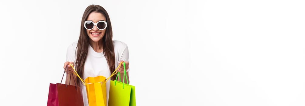 Shopping, leisure and lifestyle concept. Portrait of excited happy young girl likes shop, attend favorite mall, got lots of new clothes, bragging it, open up bag to show friend, smiling enthusiastic.