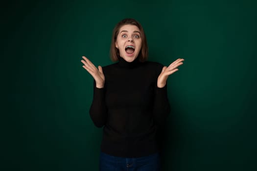 A woman wearing a black sweater is shown with a surprised expression on her face. Her eyebrows are arched, eyes wide open, and mouth slightly agape, indicating shock or disbelief.