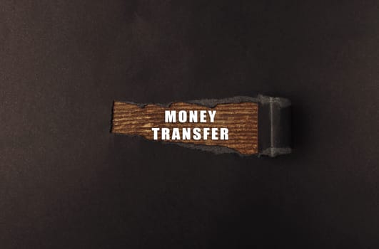 A wooden sign with the words money transfer written on it. The sign is placed on a black background, which creates a sense of mystery and intrigue